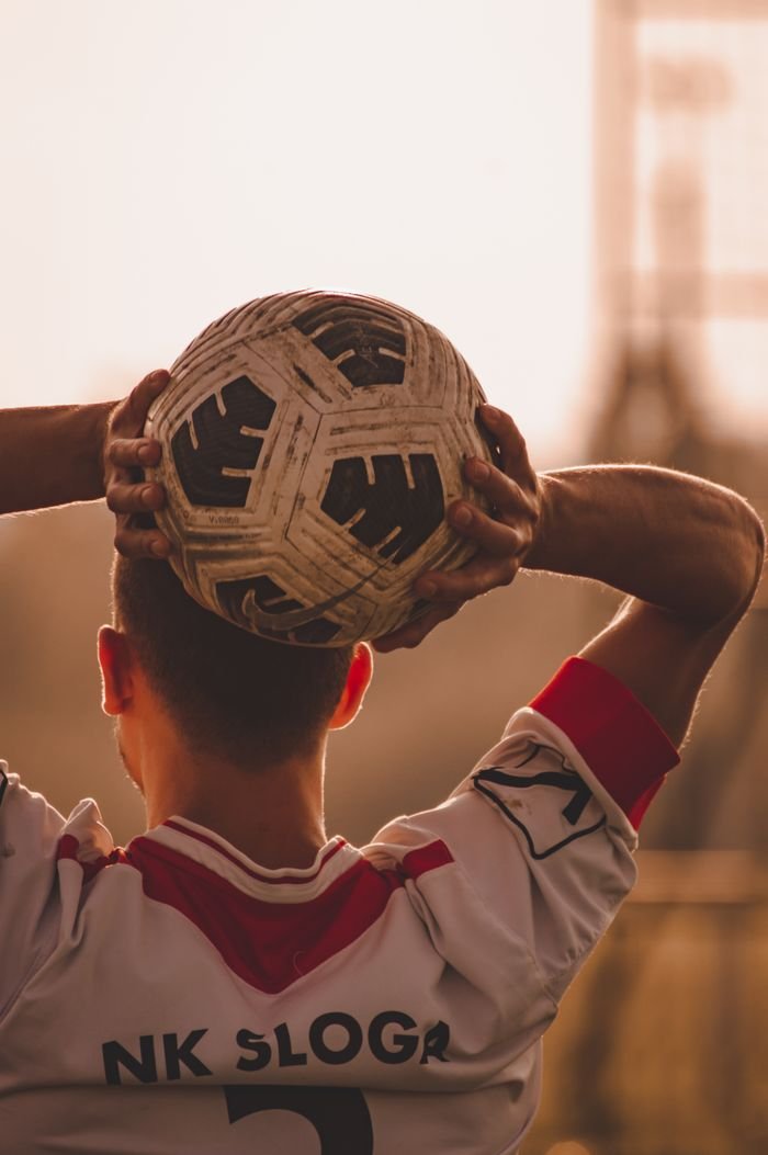 Back view of a soccer player holding a ball, ready for a throw-in on the field.