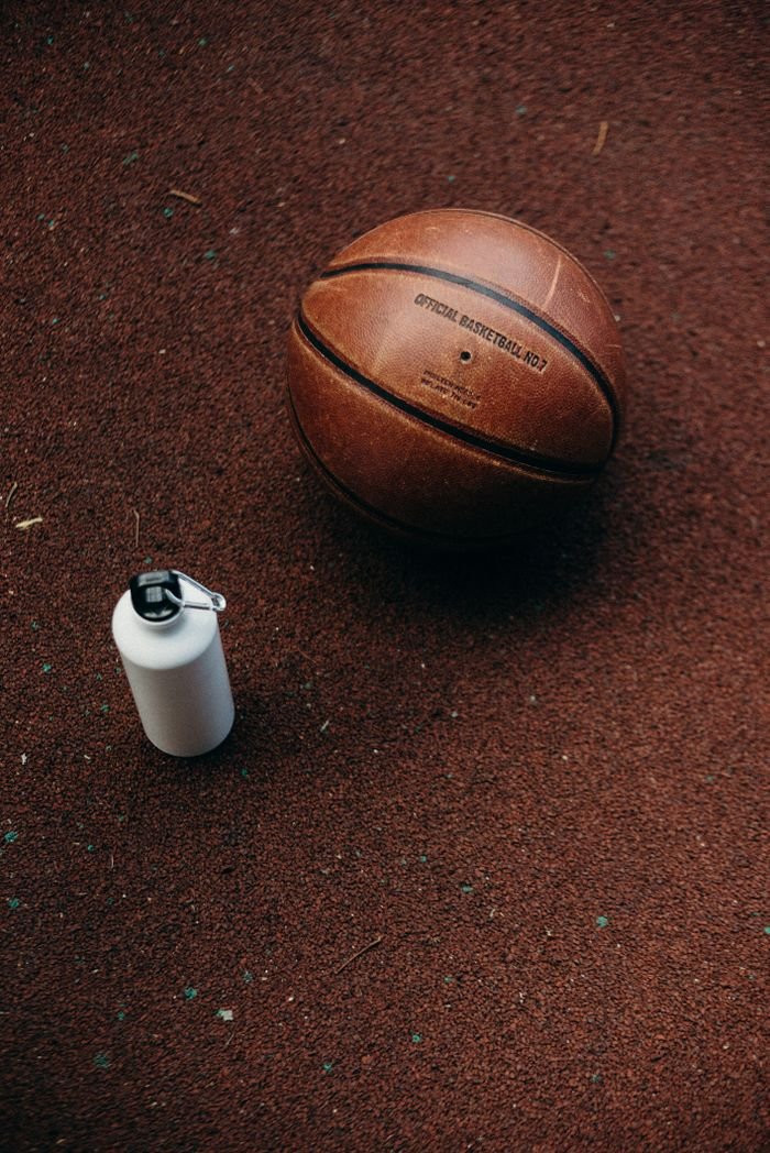 Close-up of a basketball and a water bottle on a textured court surface, ideal for sports content.
